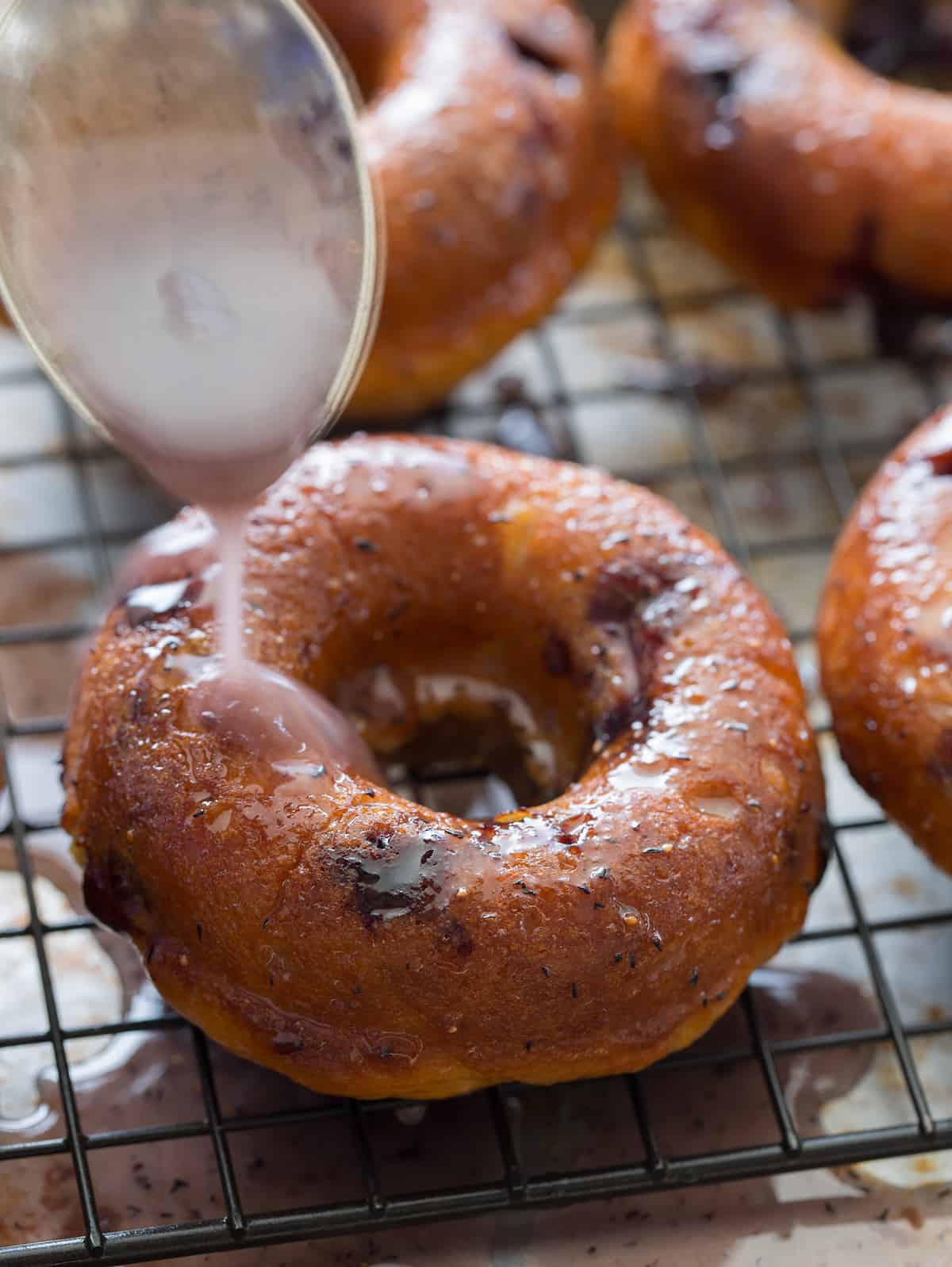 Baked blueberry donuts on a baking sheet being drizzled with a glaze.