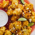 A close up of elote fritters with lime wedges and a ramekin of cilantro mayo.