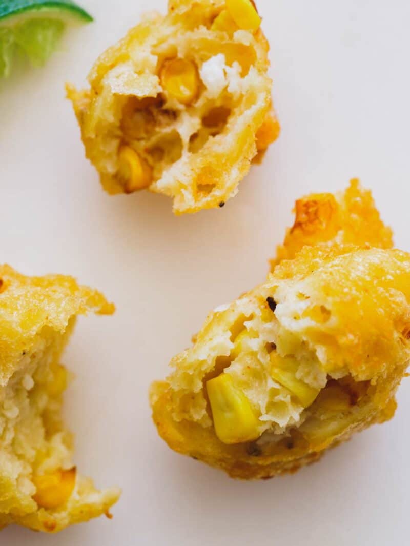 A close up of elote fritters broken open to reveal corn inside.
