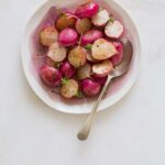 A bowl of roasted radishes with a spoon.