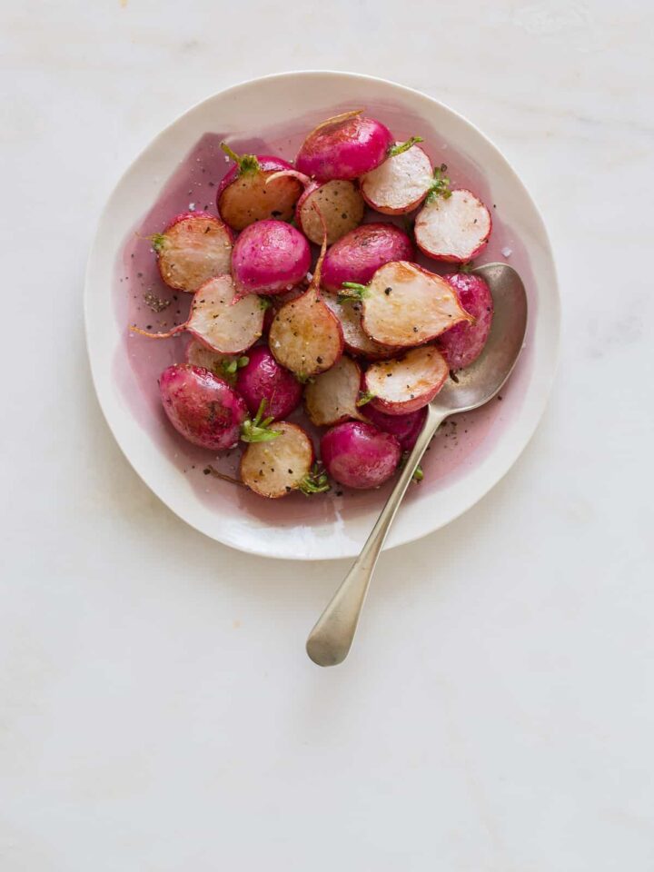 A bowl of roasted radishes with a spoon.