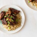 Plates of honey soy braised ribs over brown rice with thinly sliced green onions.