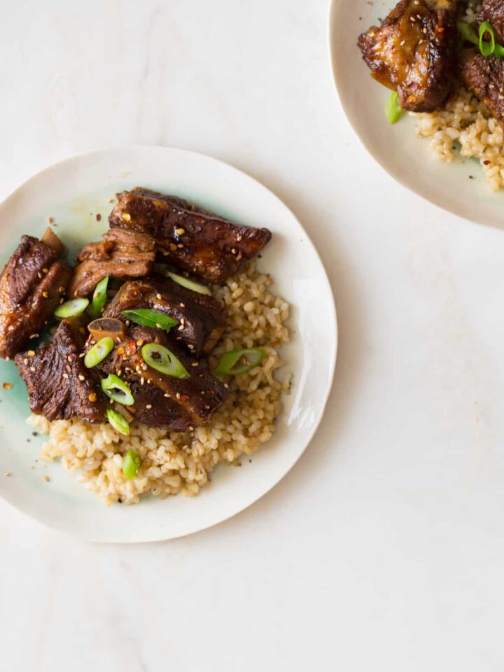 Plates of honey soy braised ribs over brown rice with thinly sliced green onions.