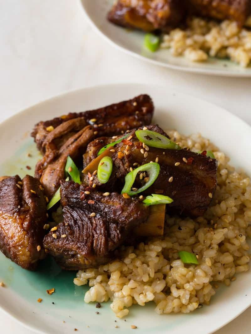 A close up of honey soy braised ribs over brown rice with thinly sliced green onions.