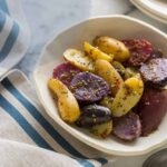 A bowl of warm German potato salad with a blue striped napkin.