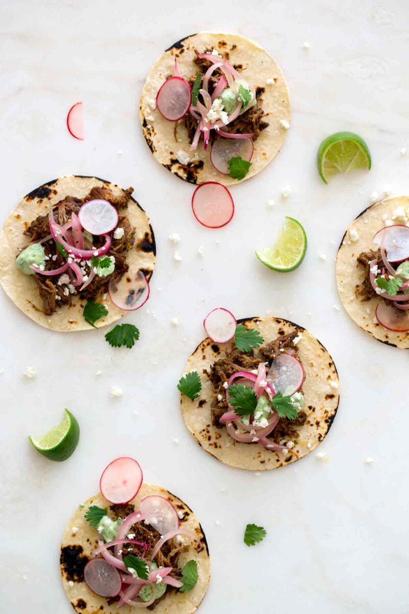 Several cochinita pibil tacos with radishes and lime wedges.