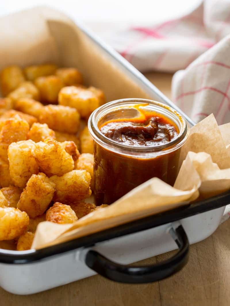 A tray of tater tots with a glass jar of sweet and tangy BBQ sauce.