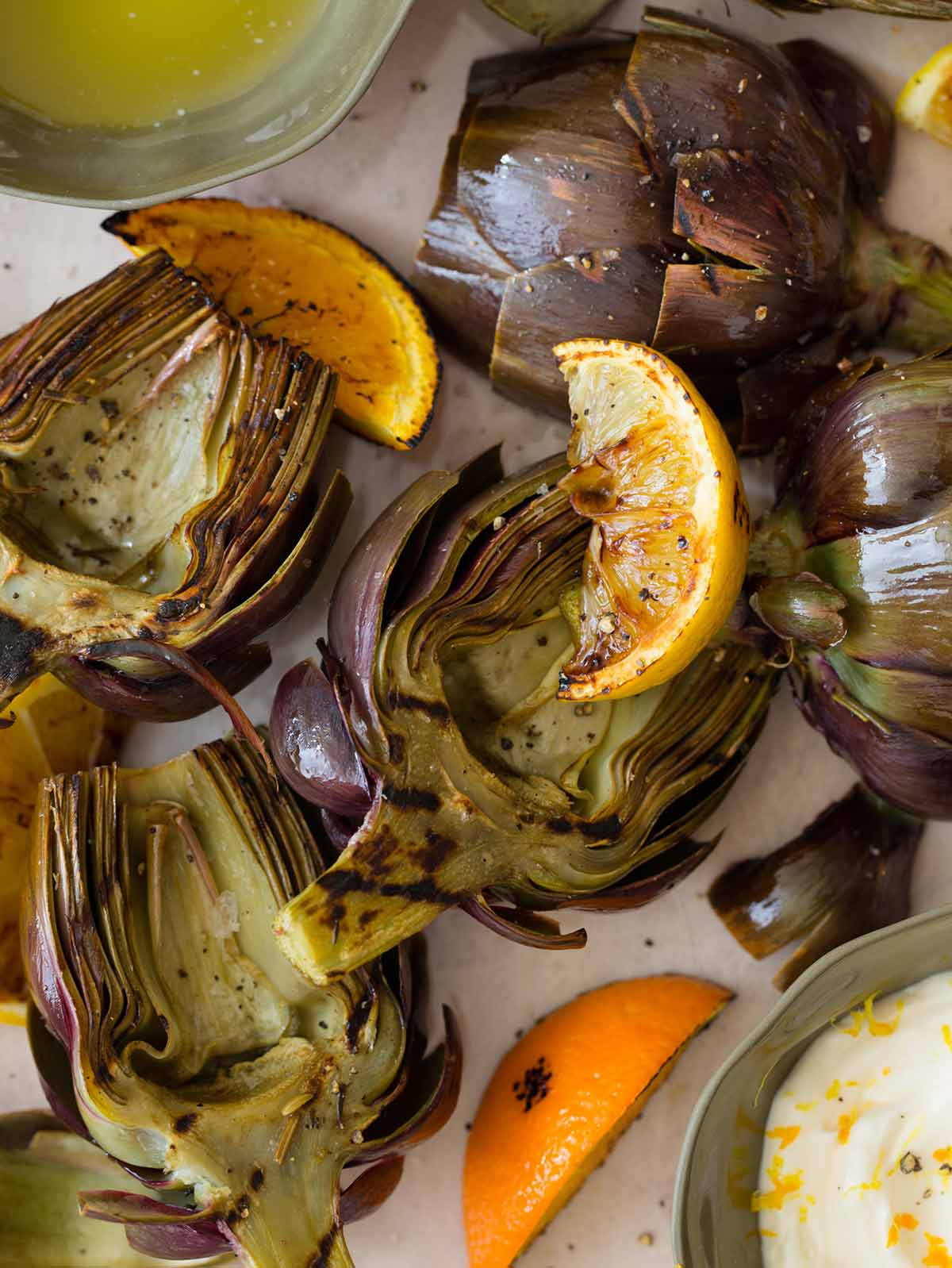 Grilled Artichokes on a platter with melted butter and aioli.