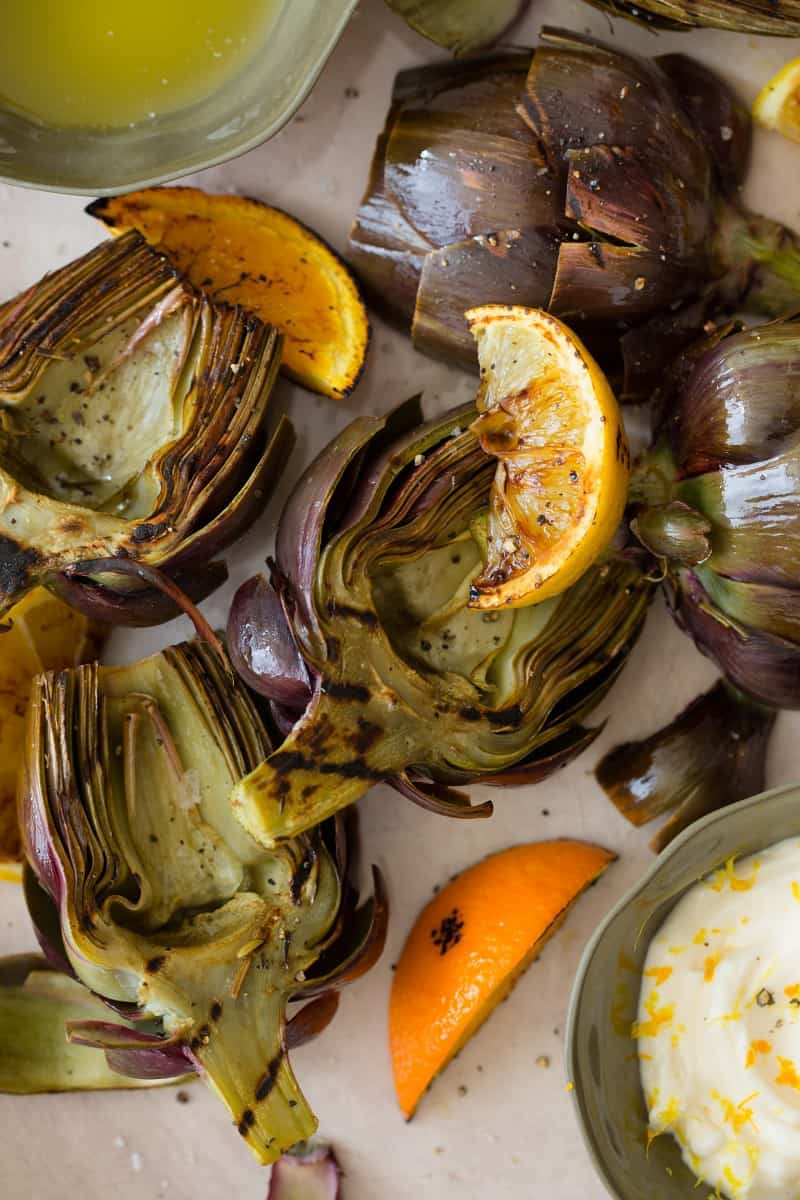 A close up of grilled artichokes with orange and lemon wedges and aloe on the side.