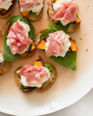 Grilled peach and burrata crostini on a platter.