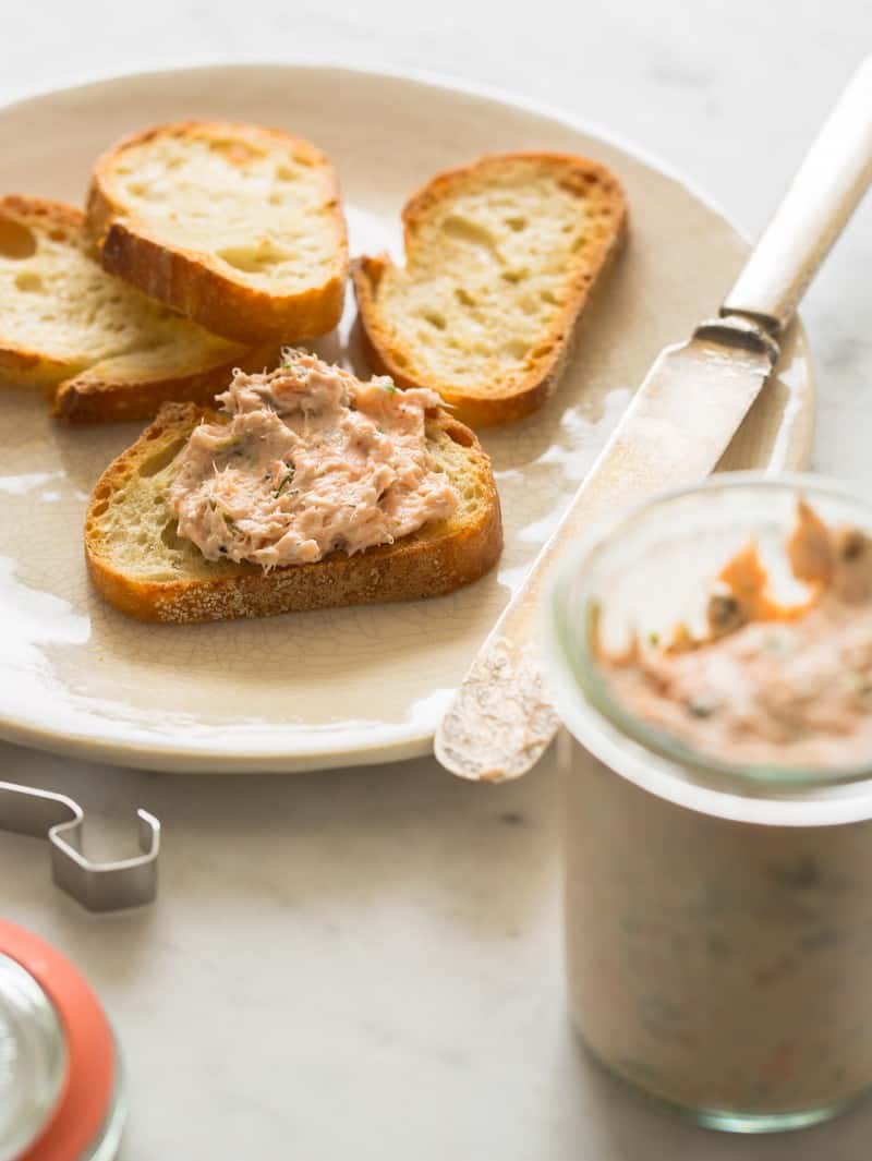 Salmon rillettes on crostini next to a jar and a knife.