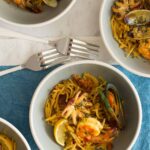 Seafood fideua in bowls with forks and linens.