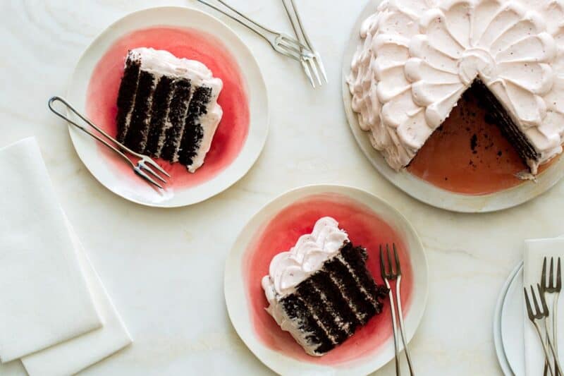 A whole devils food cake with real strawberry frosting next to slices on plates with forks.