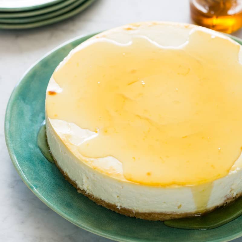 A goat cheese and yogurt cheesecake drizzled with honey with extra plates.