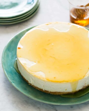 A goat cheese and yogurt cheesecake drizzled with honey with extra plates.
