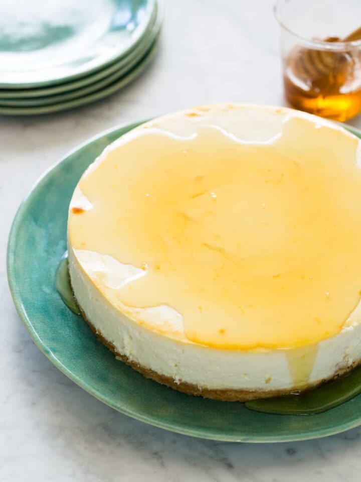 A goat cheese and yogurt cheesecake drizzled with honey with extra plates.