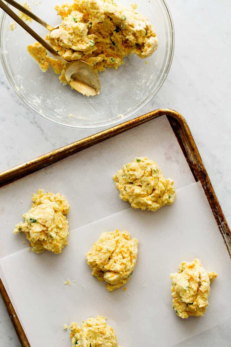 scooping Cornmeal and Jalapeño Cheddar Biscuits dough onto a baking sheet. 