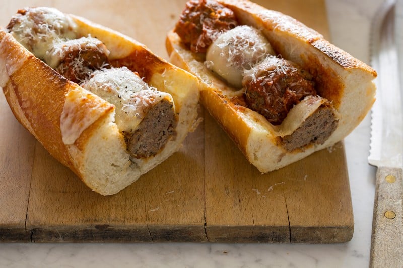 A meatball sub cut in half to see the meatballs on a cutting board. 