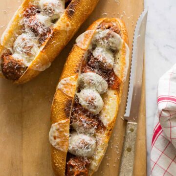 Mega meatball sub sandwiches on a wooden cutting board with a knife and linen.