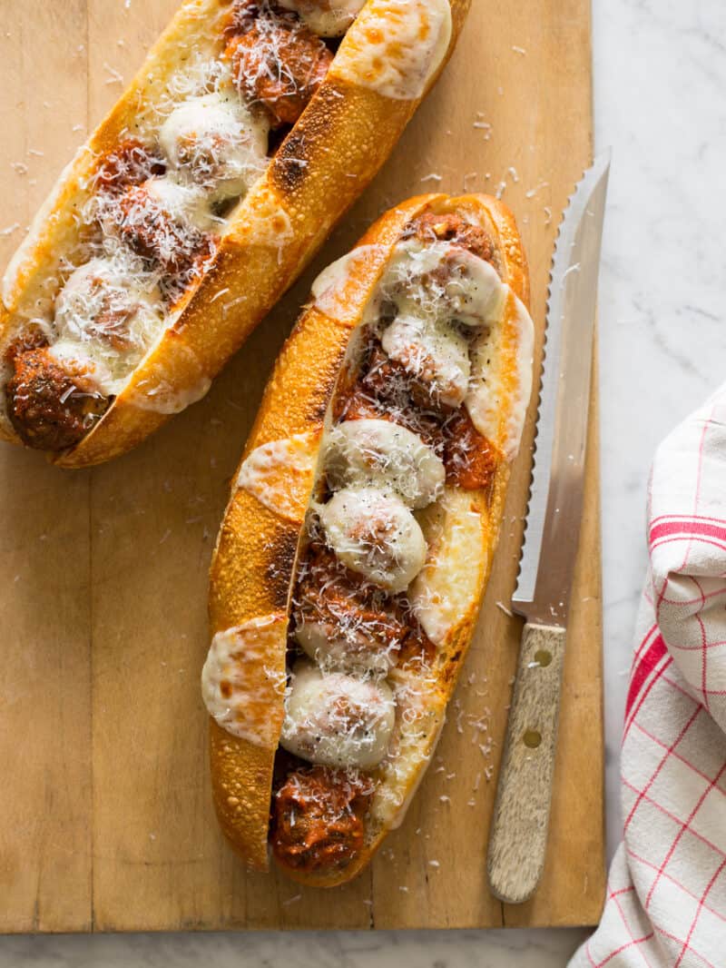 Mega meatball sub sandwiches on a wooden cutting board with a knife and linen.