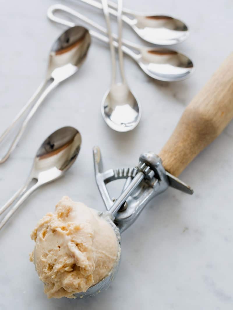 A scoop of salty nuts ice cream next to a pile of ice cream spoons.