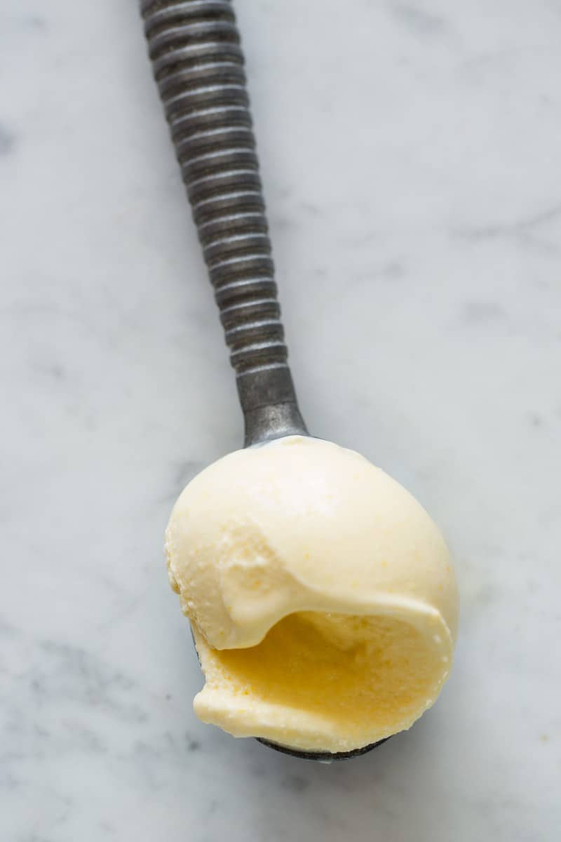 A close up of an ice cream scooper full of sweet corn ice cream.