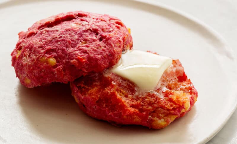A cheesy beet biscuit cut in half with a pad of melted butter on it.