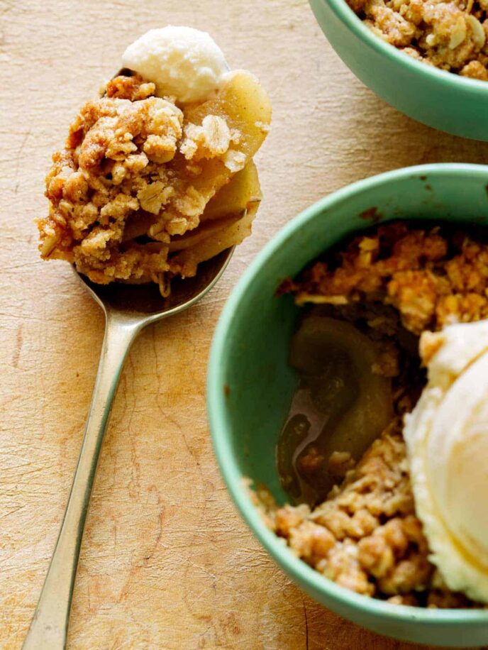 A close up of an individual apple crisp a la mode next to a spoonful.