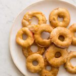 A plate of stacked apple fritter rings with vanilla bean glaze.