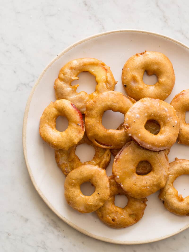 A plate of stacked apple fritter rings with vanilla bean glaze.