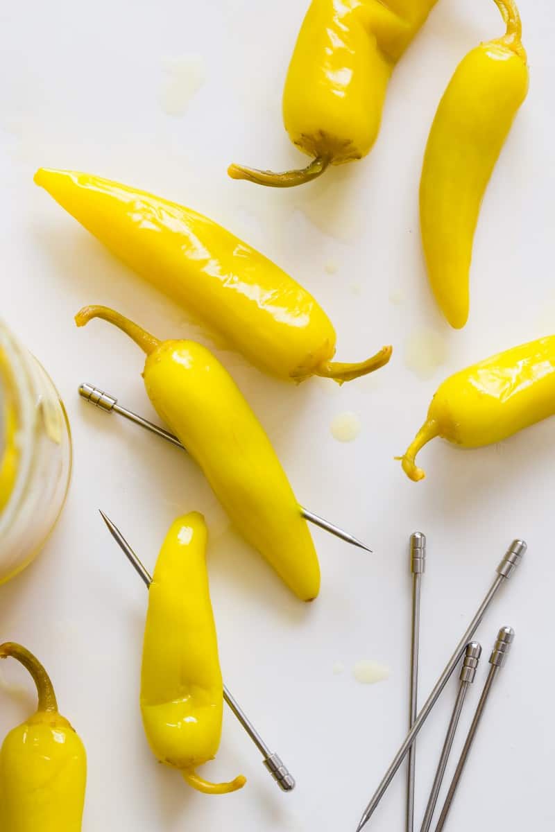 A close up of pickled peppers with steel cocktail picks.