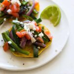 A close up of a plate cachapas topped with veggies and a lime wedge.