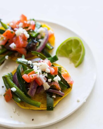 A close up of a plate cachapas topped with veggies and a lime wedge.