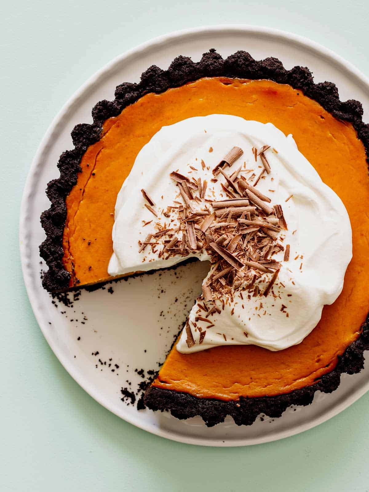 A whole pumpkin pie with chocolate crust and whipped cream with a slice taken out.