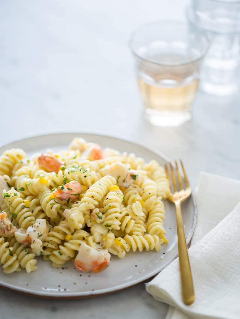 Lobster and corn pasta on a plate with a glass of wine in the background.