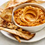 A close up of savory pumpkin hummus on a plate with baked pita chips.