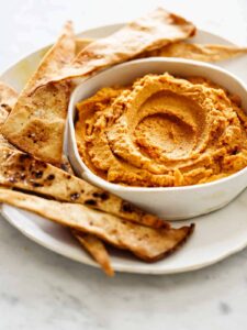 A close up of savory pumpkin hummus on a plate with baked pita chips. 