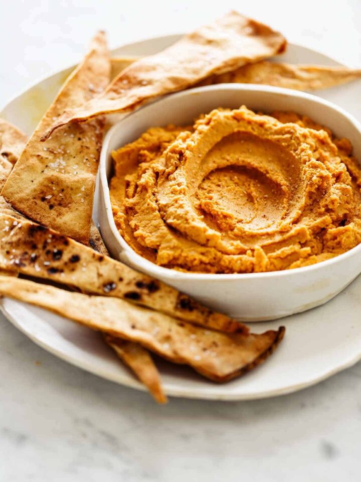 A close up of savory pumpkin hummus on a plate with baked pita chips.