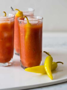 Several simple bloody marys garnished with pickled peppers.