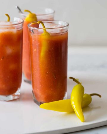 Several simple bloody marys garnished with pickled peppers.