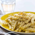 A close up of vegan cauliflower cream sauce on pasta with a fork and drink.