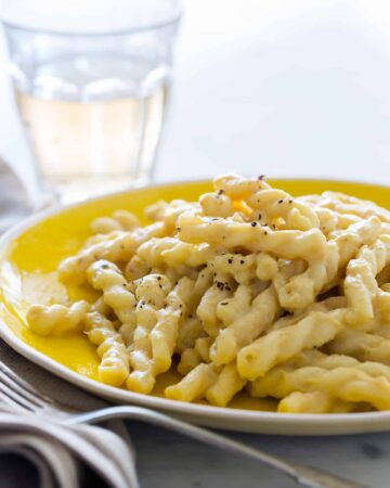 A close up of vegan cauliflower cream sauce on pasta with a fork and drink.
