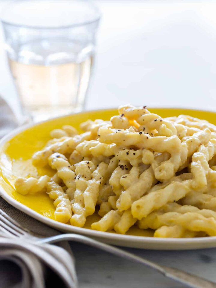 A close up of vegan cauliflower cream sauce on pasta with a fork and drink.