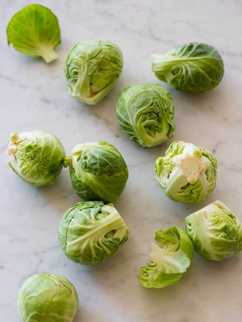 A close up of fresh uncooked Brussels sprouts on a marble surface.
