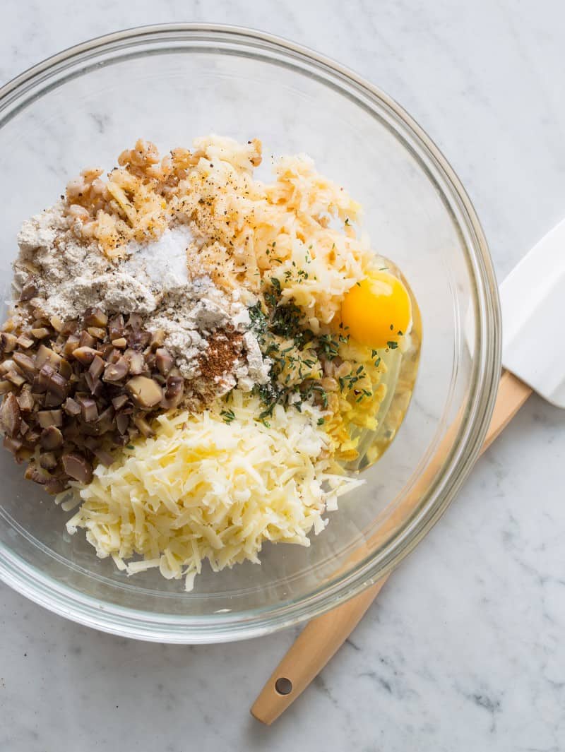 A close up of ingredients in a bowl for cheesy apple faro cakes with a spatula.