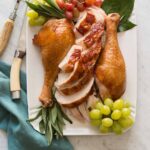 A platter of citrus and herb roasted turkey garnished with grapes and herbs with carving utensils.