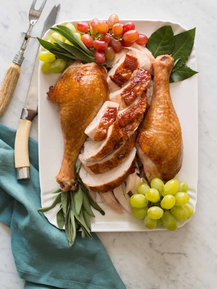 A platter of citrus and herb roasted turkey garnished with grapes and herbs with carving utensils.