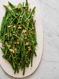 A platter of lightly roasted green beans with parmesan almond crumble.