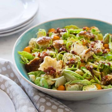 A bowl of shaved Brussels sprouts salad with a warm prosciutto mustard vinaigrette.