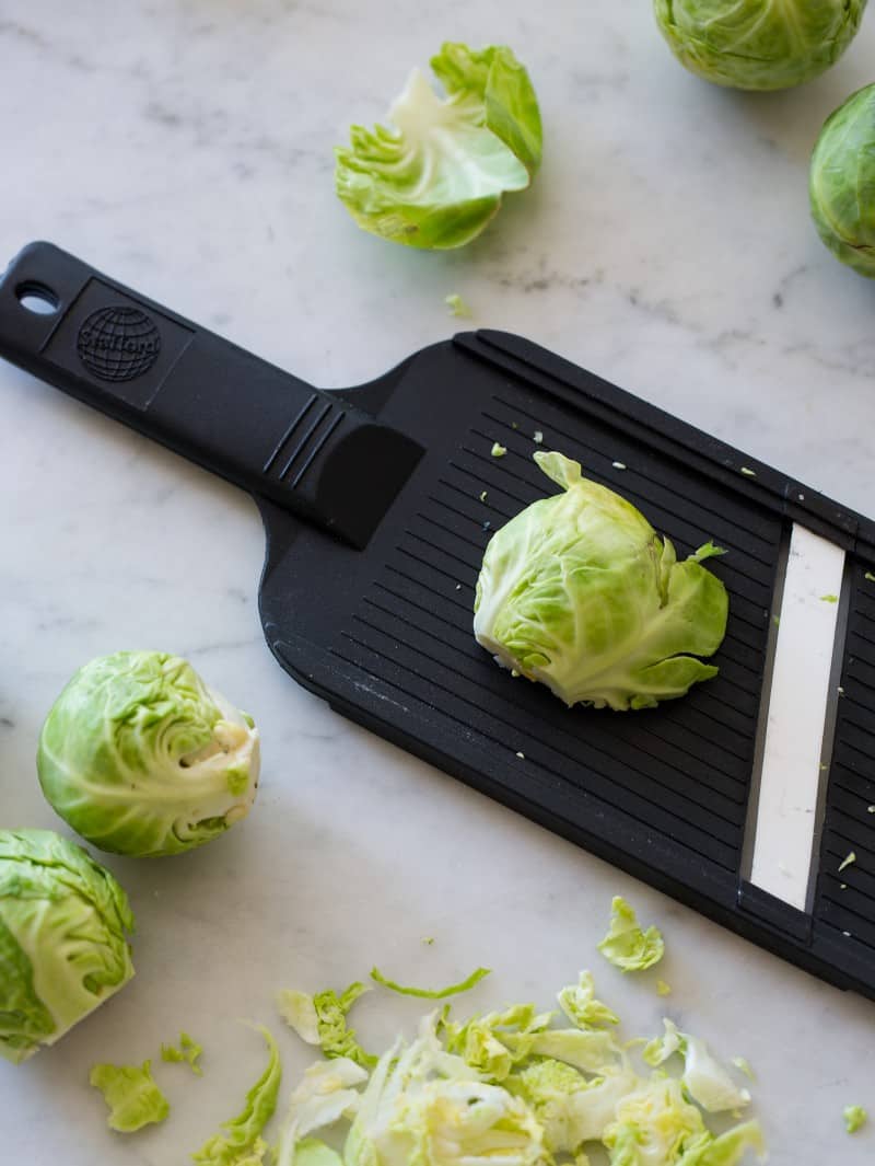 A close up of fresh uncooked Brussels sprouts being shaved on a mandolin.